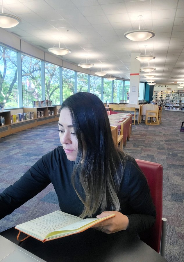 Marisol investigando en la biblioteca, libreta en mano